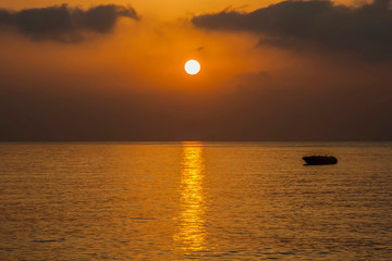 
Early sea morning, the sun is low above the horizon, a calm sea, a sunny path on the water, a lonely boat drifts.