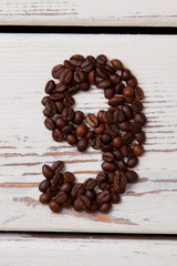 Brown roasted coffee beans arranged in a shape of nine. Seeds in a form of number nine on white wood.
