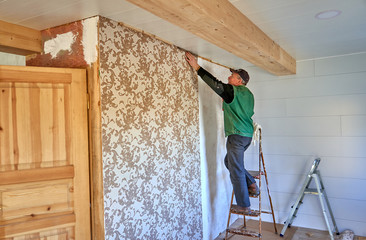 Fototapeta premium Construction worker on a ladder to glue wallpapers 