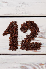 Coffee beans in a shape of number twelve on white surface. Brown roasted seeds on wooden planks forming 12 number.