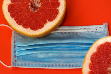 Grapefruits and a medical protective mask on an orange background. Vitamin c supplement, benefits for health. Disease prevention during quarantine. Antivirus concept.