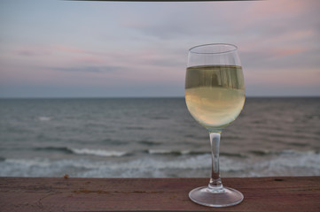 Glass of white wine in the sunset overlooking the sea. Glass of wine on the wooden jetty at sunny sea.