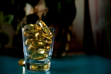 A glass cup with omega 3 vitamins stands on a blue table near the window, near a birch tree,.