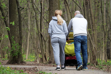Fototapeta premium Couple with a baby stroller walking in spring park. Quarantine in a city during covid-19 coronavirus pandemic, concept of motherhood, parents with pram
