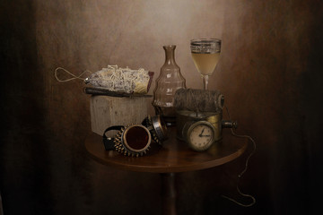 Gruppo di oggetti antichi sul tavolo,con vaso di vetro, vino,salame e orologio.