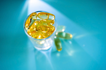 A handful of omega 3 capsules with a glass beaker on a blue background.