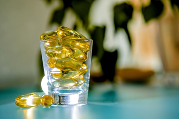 A glass cup with omega 3 vitamins stands on a blue table near the window, near a birch tree,.