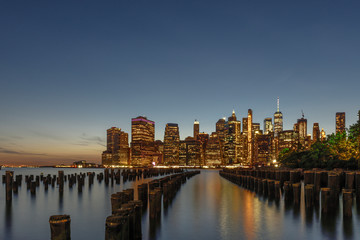 Fototapeta na wymiar Blick über den East River nach Manhattan zur Abenddammerung in Langzeitbelichtung-im Vordergrund Holzpfähle