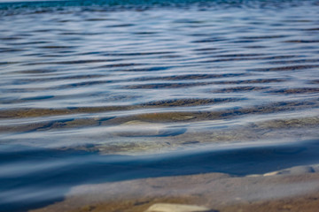 The surface is salty sea water, swaying in small waves near the shore, through the transparent bottom you can see stones and pebbles
