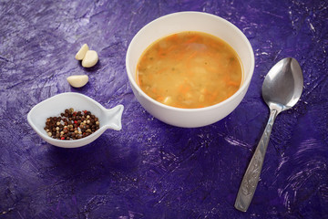 Bowl of orange carrot and potato soup, garlic, pepper in decorative plate on the violet textured background. Delicious lunch dish, healthy food. 