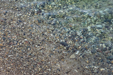 The surface is salty sea water, swaying in small waves near the shore, through the transparent bottom you can see stones and pebbles
