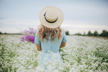 beautiful blonde girl in a field of daisies. woman in a blue dress in a field of white flowers....