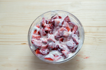 glass bowl with strawberries with cream isolated on wooden background