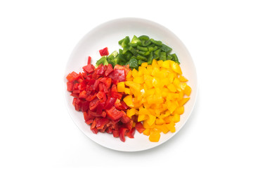 Closeup of various colors of cutted pieces of organic peppers in a white plate on white background on top view