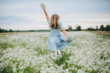 Naklejka na ściany i meble beautiful blonde girl in a field of daisies. wreath of wildflowers on his head. woman in a blue dress in a field of white flowers. charming girl with a bouquet of daisies. summer tender photo