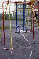 The playground is in quarantine due to the coronavirus pandemic. Warning Red and white ribbons are torn by bad citizens on a swing.