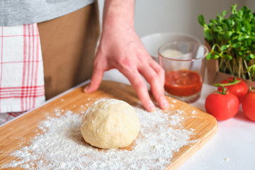 A man is preparing pizza dough. Men's hands in flour. Cooking homemade italian pizza. Preparation raw ingredients for baking. Fresh natural healthy food. Сulinary сhef kneading dough on kitchen table