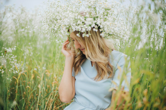beautiful blonde girl in a field of daisies. wreath of wildflowers on his head. woman in a blue dress in a field of white flowers. charming girl with a bouquet of daisies. summer tender photo