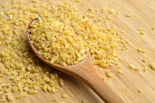 Cracked wheat daliya grains in wooden spoon, on bamboo cutting board