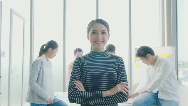 Portrait of young Asian businesswoman smiling confidently toward camera standing in front of office colleagues in the meeting room, office worker lifestyle, working women, startup entrepreneur.