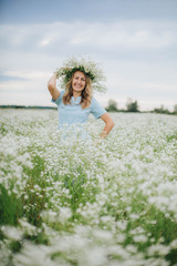 Obraz na płótnie Canvas beautiful blonde girl in a field of daisies. wreath of wildflowers on his head. woman in a blue dress in a field of white flowers. charming girl with a bouquet of daisies. summer tender photo