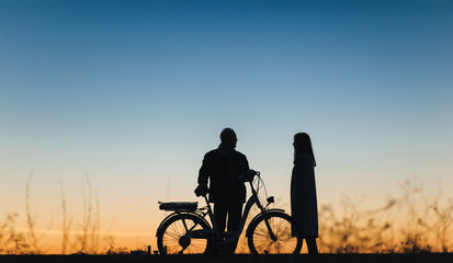 Fototapeta na wymiar Silhouette of a girl and man on the e-bike or electric bicycle on the sunset background. Country style, transportation in the village. Copy space.Travel, father and daughter.