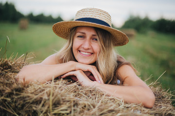 beautiful girl in a straw hat on a field with straw bales. girl sitting on the hay. blonde in the summer in a field with a hat. life in the countryside, outdoors. eco project. clean environment