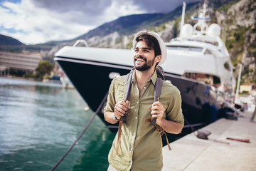 Young man walking by the harbor of a touristic sea resort with boats on background