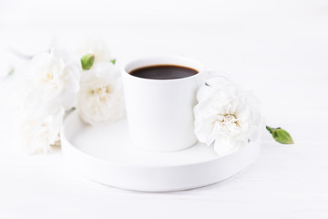 Obraz na płótnie Canvas White cup of black coffee and carnations flowers on a white background, copy space