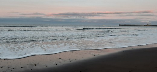 Sandy beach view with waves at sunset in Whitby, North Yorkshire