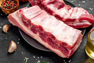 raw pork ribs with spices in a black plate on a stone background 