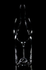 Silhouette of a transparent glass bottle with a glass of wine behind with black background