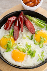 Fried eggs with sausages and onion on frying pan with sauce