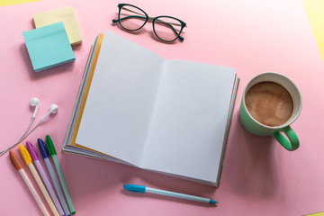 Notebook, pens, mug with coffee, glasses, and headphones on the pink background. Layout design with copy space. To do list.
