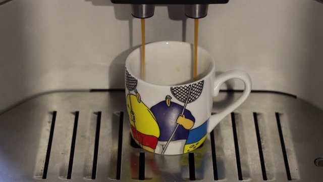 Espresso zu Hause mit einem Kaffevollautomat in eine bunte Tasse mit zwei dicken M&auml;nnern zubereiten 