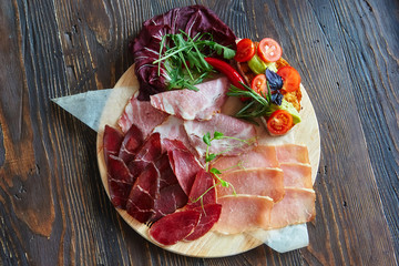 A variety of meat products, laid out on a wooden Board close-up, horizontally, are next to bruschetta with vegetables and fresh herbs