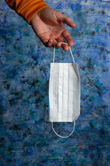 medical mask in a male hand on a blue background