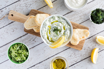 A top down view of tzatziki dip garnished with lemon and dill and surrounded by ingredients used to make the dip.