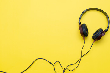 Modern headphones with cables on yellow background.