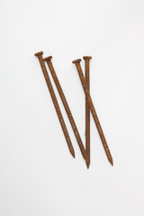 Group of four long rusty nails against plain white background