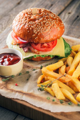 Fresh tasty burger and french fries with sauce on wooden cutting board with wood background