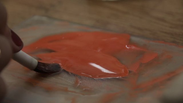 Artist's palette with orange paint. A woman's hand dips into the paint with a brush. Close up. Grayscale.