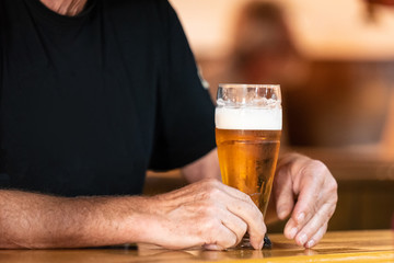 a big glass of beer on a wooden bar and a man's hand, close up