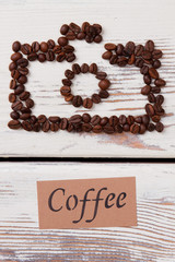 Coffee beans on the table arranged in a shape of photo camera. White planks on background.
