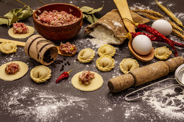 Composition with raw dumplings and ingredients on trendy black stone concrete background. Process of cooking