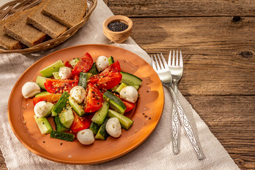 Fresh salad from tomato, cucumber and baby mozzarella. Sunny lunch with crusty bread