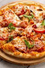Tasty pizza with ham, mushrooms, tomatoes and arugula on wooden cutting board on white background.