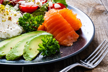 Breakfast - smoked salmon, cottage cheese, avocado and vegetable salad on wooden table
