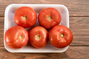 Many fresh red tomatoes on a white tray from supermarket with wooden background