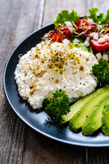 Breakfast - smoked salmon, cottage cheese, avocado and vegetable salad on wooden table
